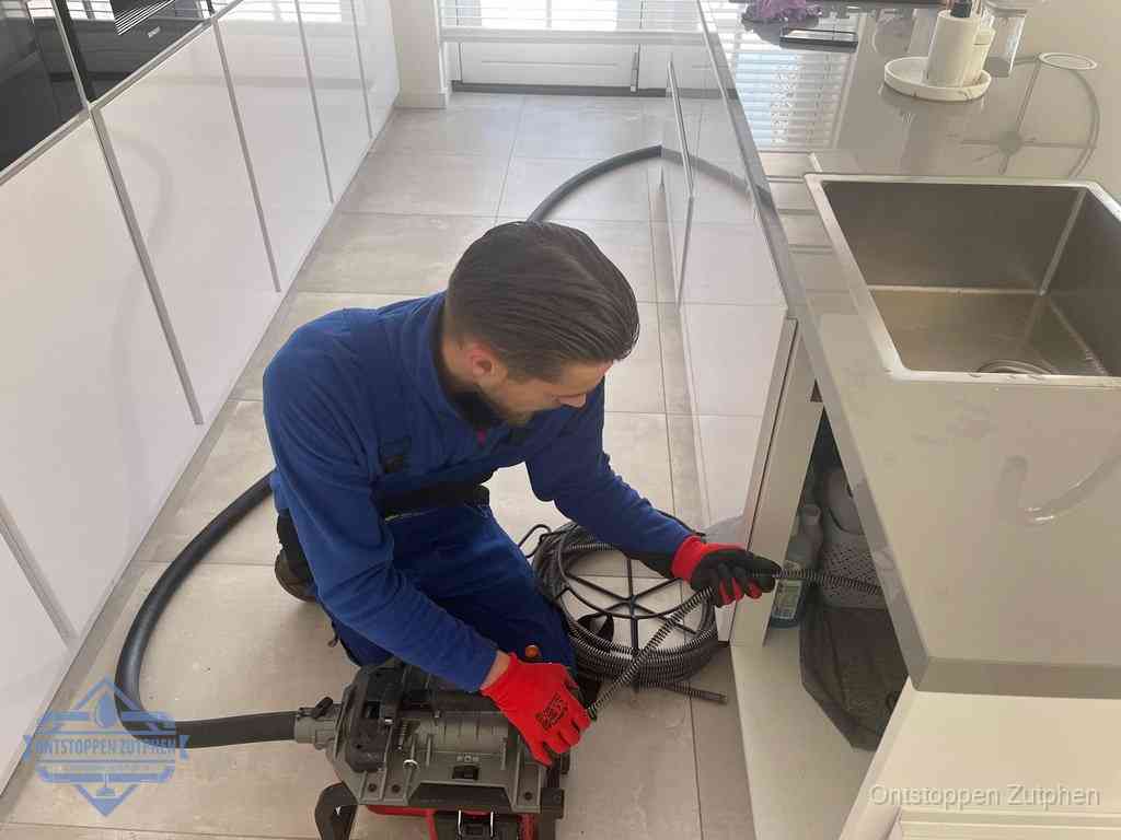 Een monteur ontstopt de keukenafvoer onder de spoelbak met een elektrische veermachine in Zutphen