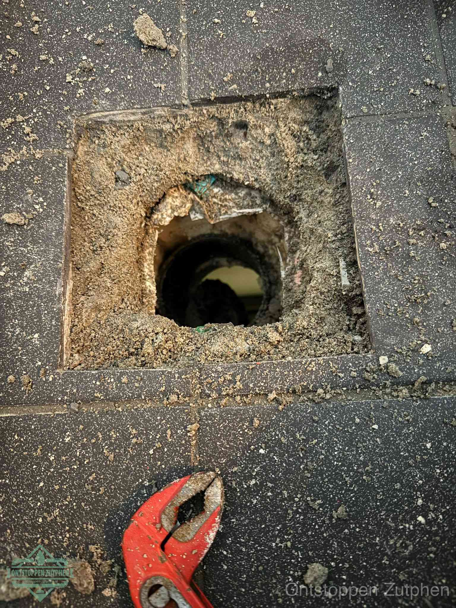 Een geopend rioolputje in een betontegelvloer met losgemaakt rooster en een zichtbare ronde afvoerbuis, het achterhalen waar de afvoerverstopping zit in Zutphen
