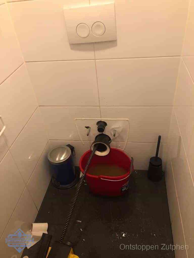 Een ontstopte wand-wc met verwijderde toiletpot waar een ontstoppingsveer in de wanduitgang verdwijnt, het achterhalen waar de verstopping zit in Zutphen