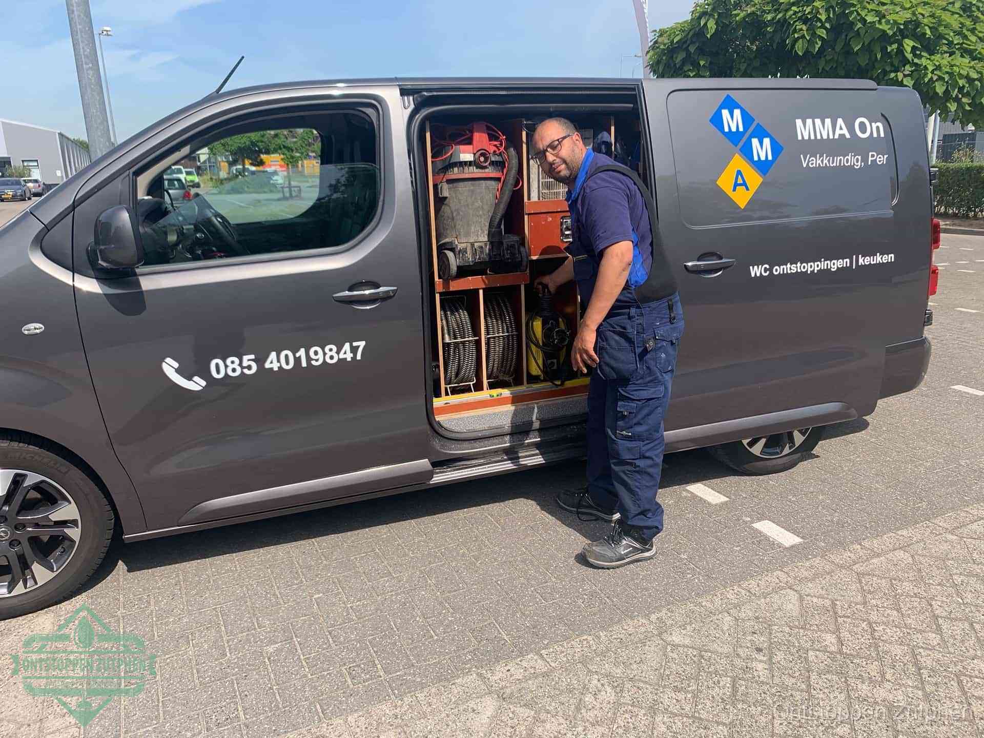 Een monteur bij de open schuifdeur van zijn bedrijfsbus op een parkeerplaats, klaar om de oorzaak van terugkerende afvoerverstoppingen aan te pakken in Zutphen