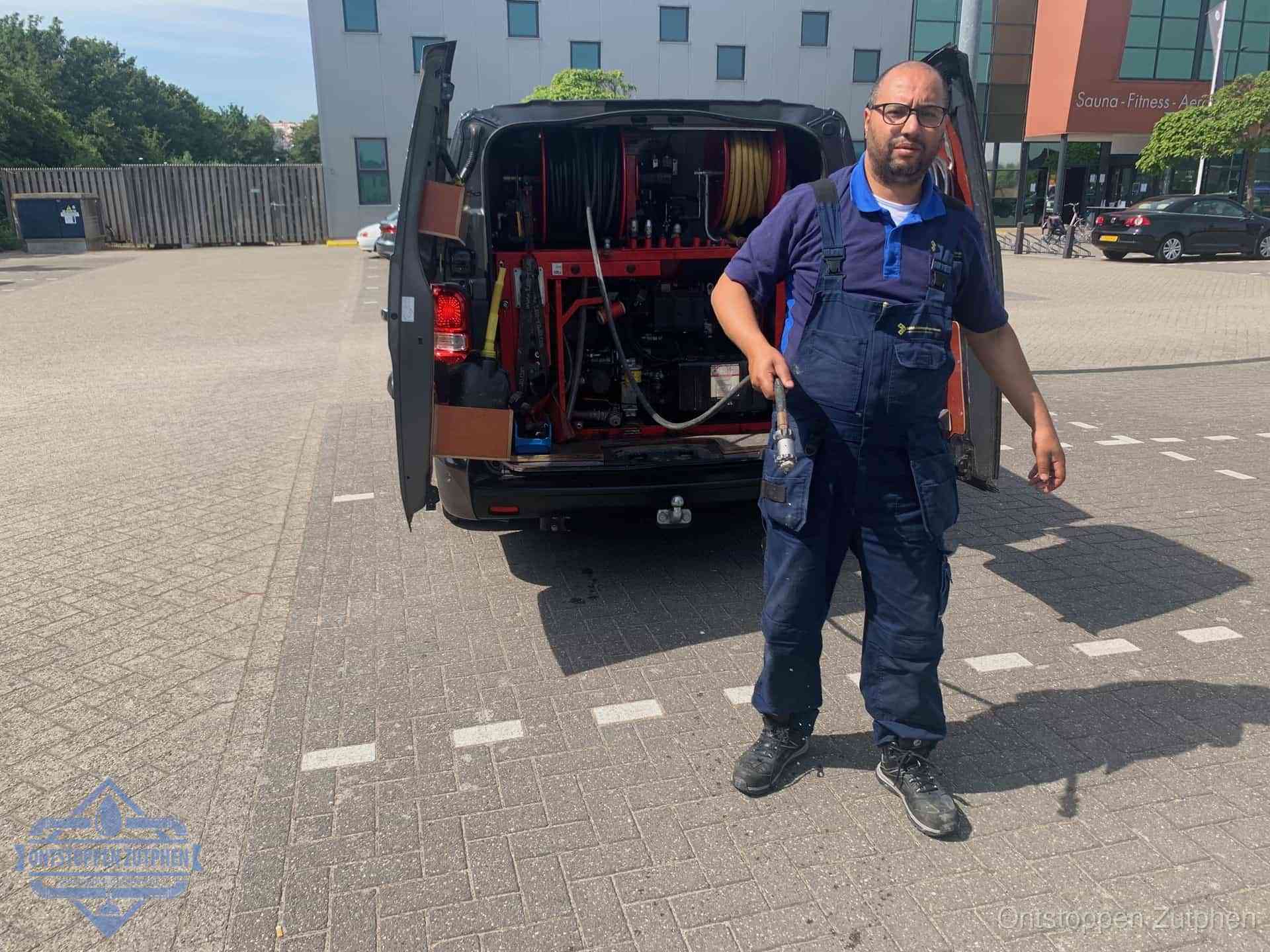 Een monteur bij zijn bestelbus met een hogedruk- en rioolreinigingsunit, klaar om de oorzaak van terugkerende wc-verstoppingen aan te pakken in Zutphen