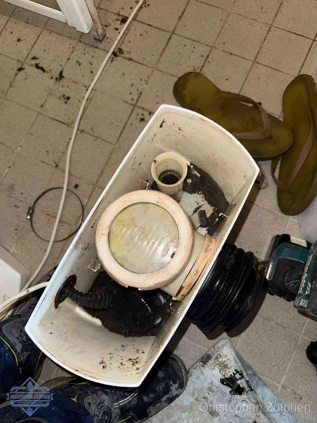 Een gedemonteerde toiletpot op de vloer met ontstoppingsveer en gereedschap ernaast, het verwijderen van een vastzittend voorwerp uit de wc in Zutphen