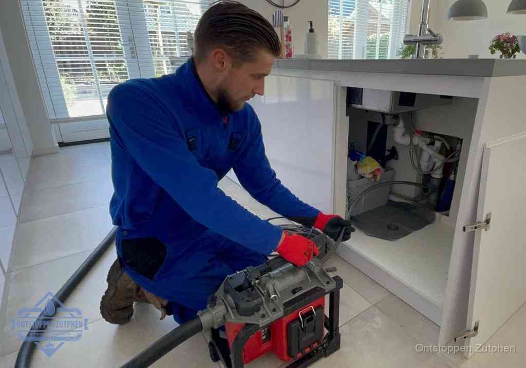 Een monteur voert een professionele elektrische ontstoppingsmachine in de afvoer onder de spoelbak tijdens het gootsteen ontstoppen in Zutphen