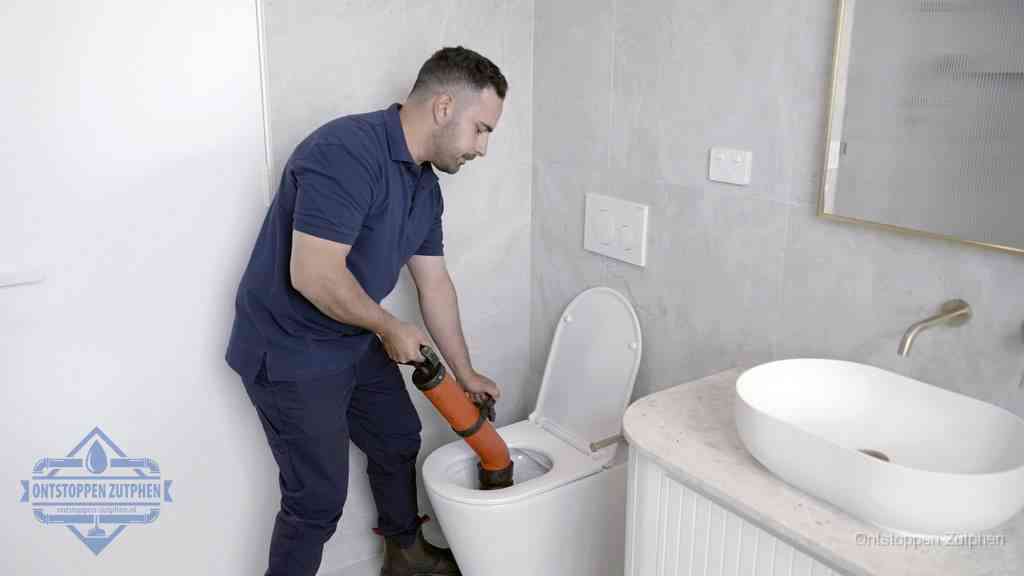 Een man gebruikt een handmatige luchtdruk-ontstopper in een modern betegeld toilet om zelf de wc te ontstoppen in Zutphen